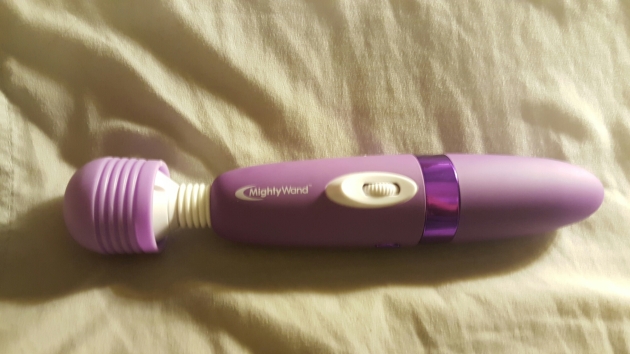 A picture of a purple mighty wand vibrator laying on a beige cloth background.